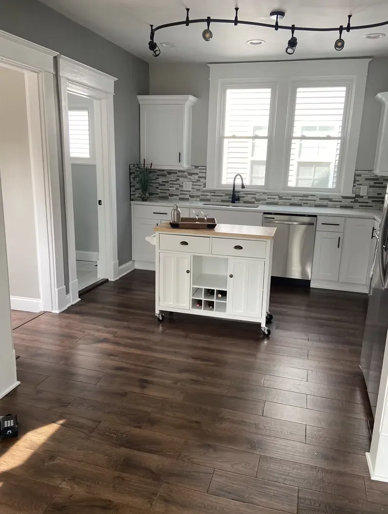 Kitchen with white cabinets, dark wood floors and a movable island cart
