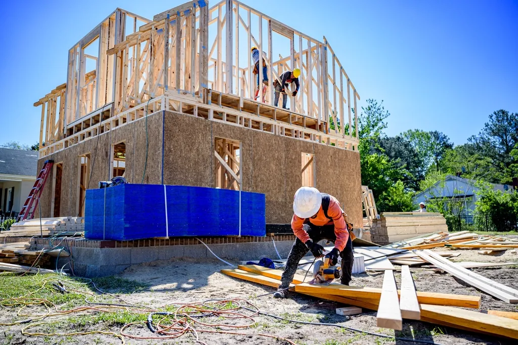 Carpenter working beside a wood framed two story house under construction