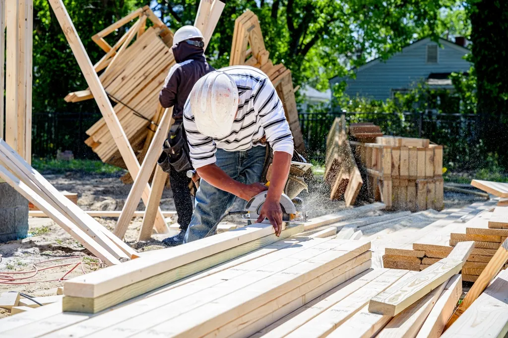 Carpenter cutting lumber on a job site with stacked boards around him