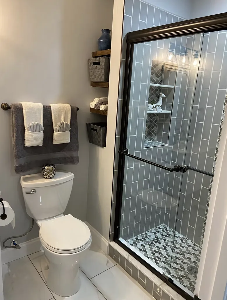 Bathroom with a glass shower, blue wall tile and a toilet with towels on the wall